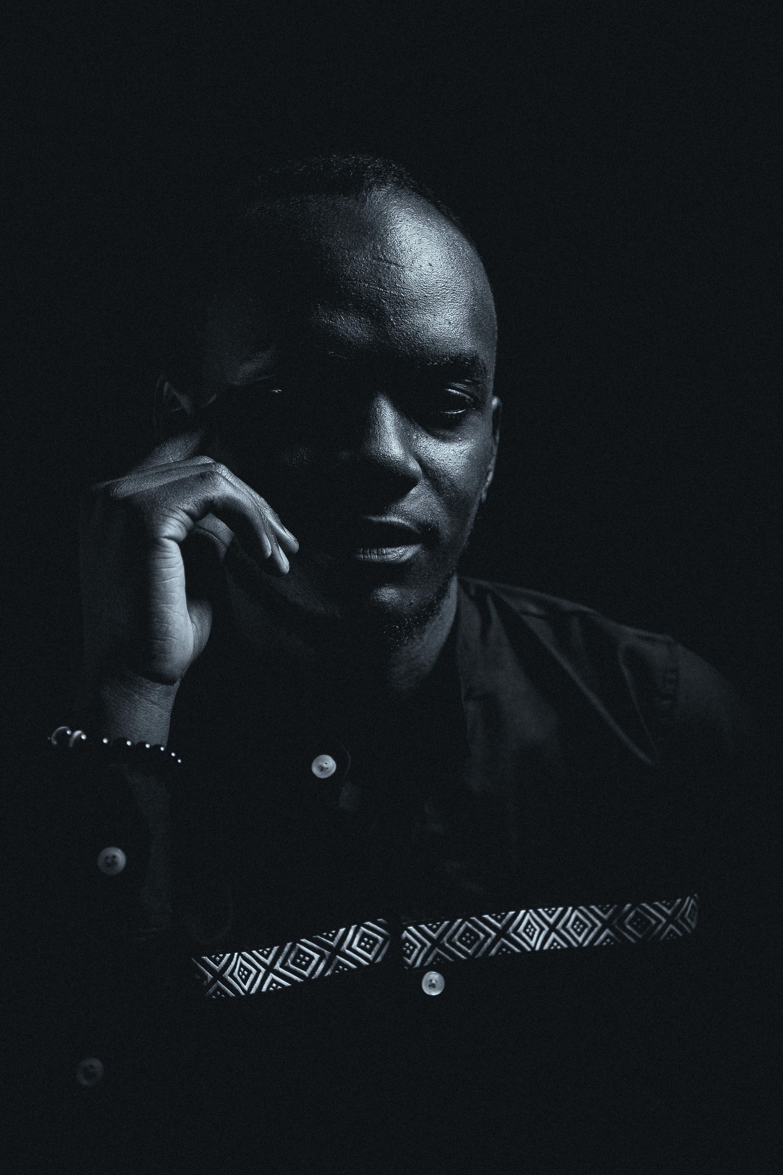 Black and white portrait of a man in a dark jacket, lit from one side, phone held to his ear
