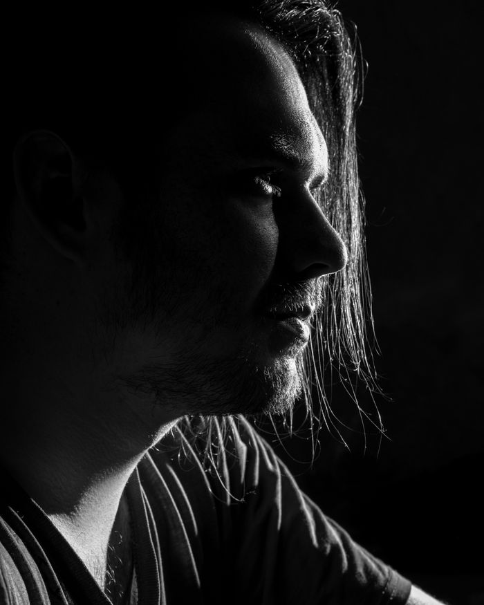 Man with long hair looking away, light catching the side of his face