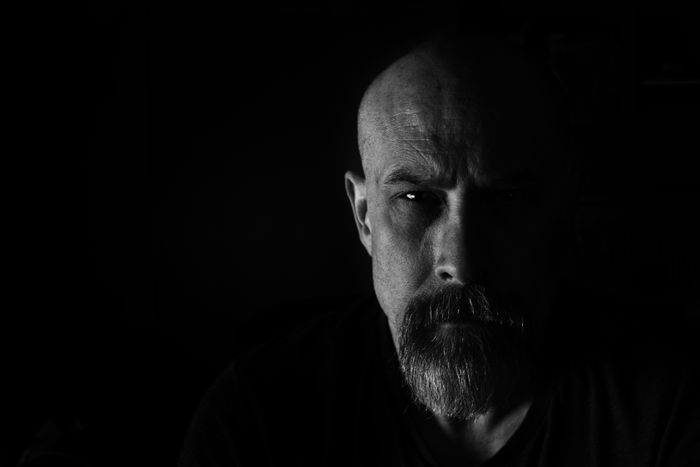 Serious bearded man with a shaved head, lit dramatically from above